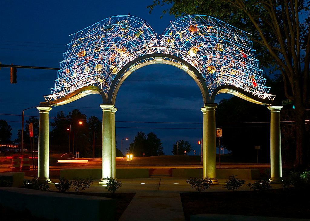 An evening shot of a gateway with wired and backlit arches in the shape of the pages of an open book.